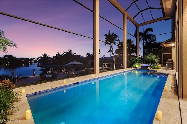 pool at dusk featuring a patio, a water view, a lanai, and an outdoor pool