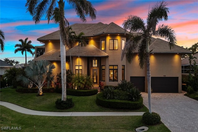 view of front of home with an attached garage, decorative driveway, a front lawn, and stucco siding