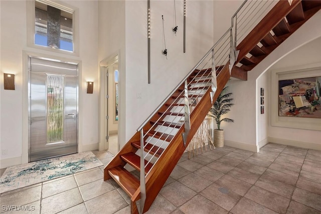 stairs featuring elevator, baseboards, and a towering ceiling