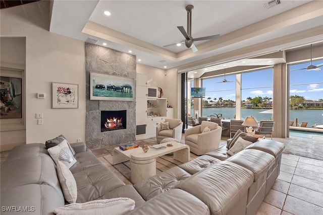 living room featuring a water view, ceiling fan, visible vents, and a tile fireplace
