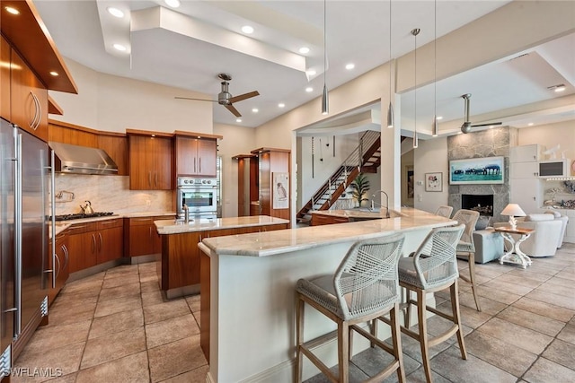 kitchen featuring wall chimney range hood, a ceiling fan, recessed lighting, stainless steel appliances, and a spacious island