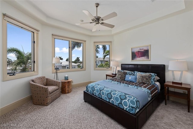 carpeted bedroom featuring a tray ceiling, ceiling fan, and baseboards