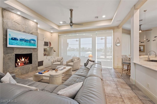 130 Hollyhock Ct, Marco Island, FL 34145 - living area featuring a ceiling fan, a tray ceiling, baseboards, and a large fireplace
