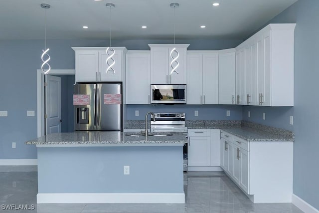 kitchen featuring appliances with stainless steel finishes, a center island with sink, a sink, baseboards, and light stone counters