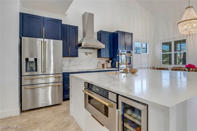 9680 Pineapple Preserve Ct, Fort Myers, FL 33908 - kitchen with appliances with stainless steel finishes, a kitchen island with sink, blue cabinetry, wall chimney exhaust hood, and wine cooler