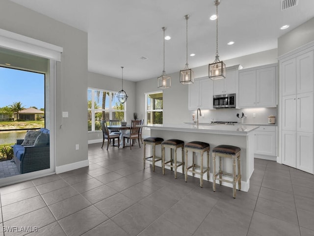 28426 Montecristo Loop, Bonita Springs, FL 34135 - kitchen featuring a kitchen breakfast bar, a kitchen island with sink, dark tile patterned flooring, light countertops, and stainless steel microwave
