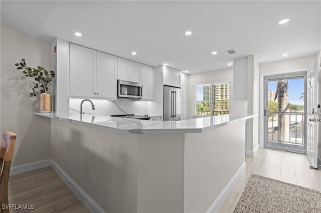 kitchen featuring stainless steel appliances, a peninsula, white cabinetry, baseboards, and recessed lighting