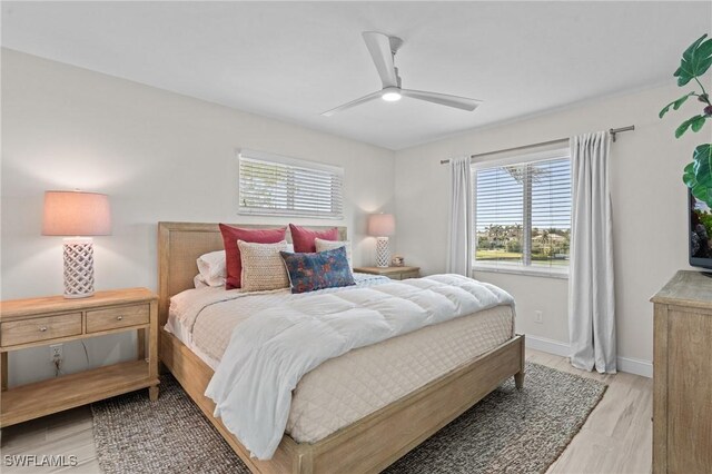bedroom with multiple windows, light wood-style floors, baseboards, and a ceiling fan