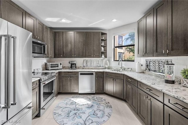 kitchen featuring open shelves, dark brown cabinets, light stone counters, a sink, and appliances with stainless steel finishes