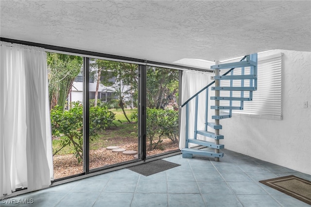doorway to outside featuring a textured ceiling, a wall of windows, a textured wall, and a wealth of natural light