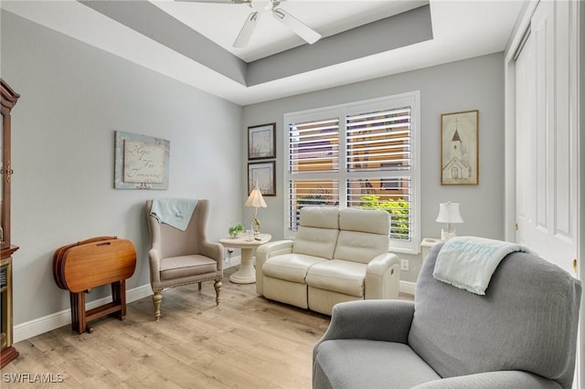 living area featuring a raised ceiling, baseboards, a ceiling fan, and light wood-type flooring