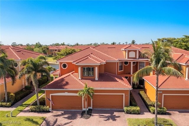 mediterranean / spanish house with a garage, stucco siding, decorative driveway, and a tile roof