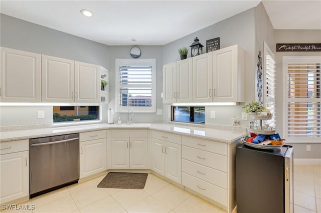 kitchen with a sink, light countertops, white cabinetry, light tile patterned floors, and stainless steel dishwasher