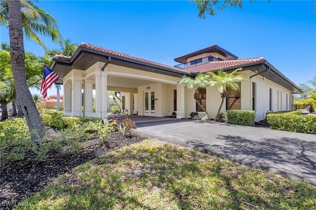 mediterranean / spanish house with stucco siding, french doors, a carport, a tiled roof, and driveway