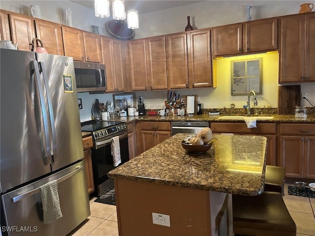 kitchen with stainless steel appliances, light tile patterned floors, a sink, and dark stone countertops
