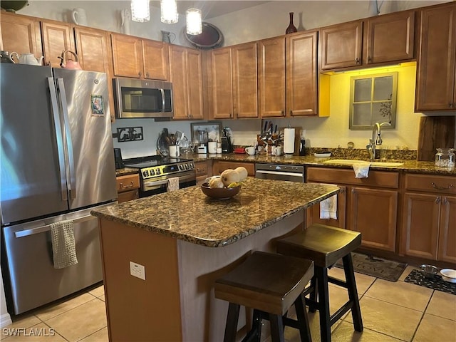 kitchen with stainless steel appliances, light tile patterned flooring, a sink, a kitchen bar, and dark stone counters