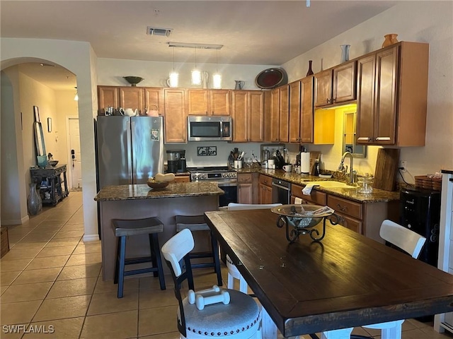 kitchen featuring appliances with stainless steel finishes, arched walkways, light tile patterned flooring, a sink, and a kitchen island