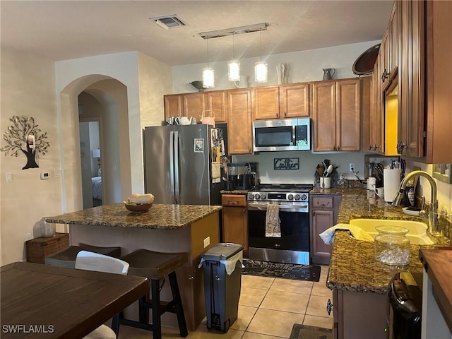 kitchen featuring stainless steel appliances, a sink, a center island, arched walkways, and brown cabinets