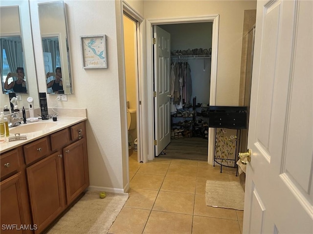 full bathroom featuring tile patterned flooring, vanity, toilet, and a walk in closet
