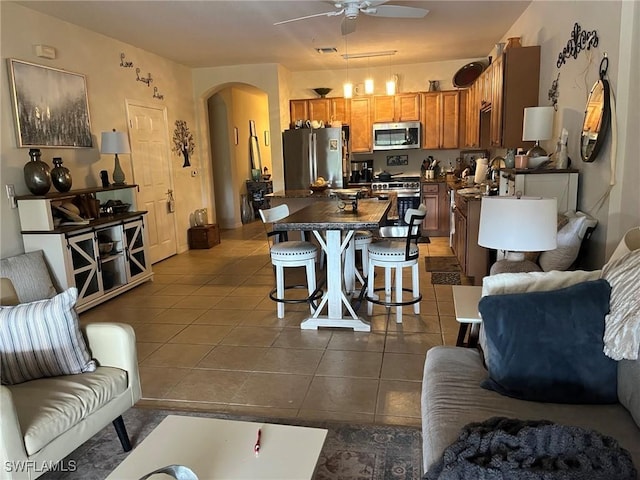 living area with arched walkways, a ceiling fan, and dark tile patterned flooring