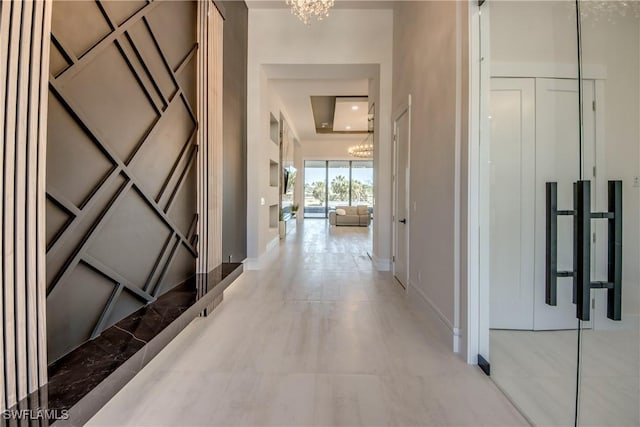 hall featuring a tray ceiling, an inviting chandelier, and baseboards