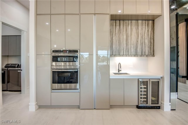 kitchen with a sink, double oven, separate washer and dryer, wine cooler, and modern cabinets