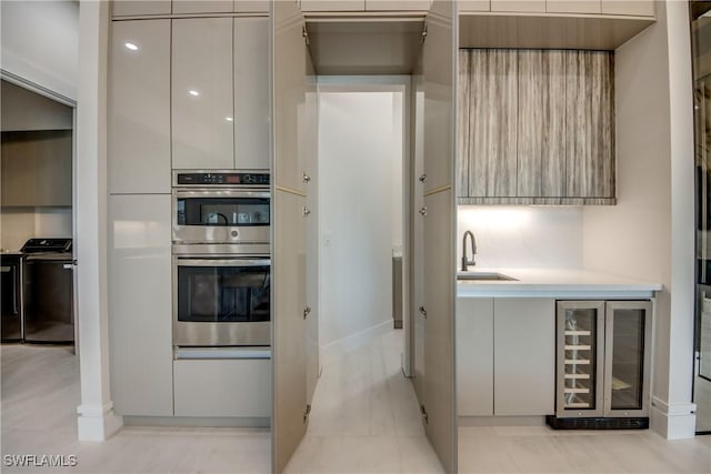 kitchen with wine cooler, double oven, modern cabinets, light countertops, and a sink