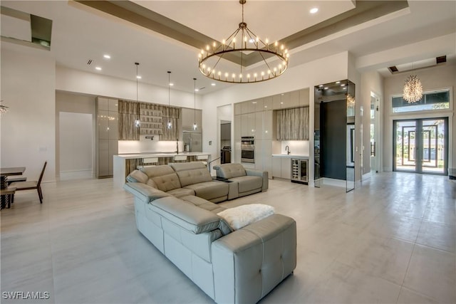 living area featuring a towering ceiling, baseboards, a raised ceiling, beverage cooler, and a chandelier