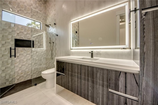 bathroom with tile patterned flooring, vanity, toilet, tile walls, and a tile shower