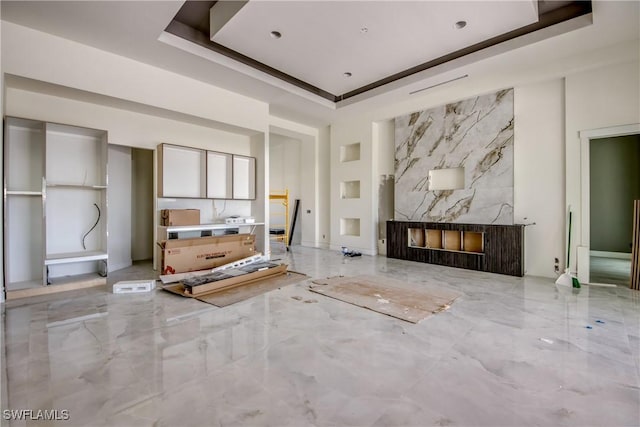 unfurnished living room with a tray ceiling, marble finish floor, and a fireplace