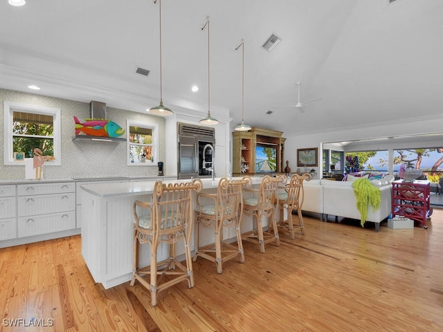 8315 Main St, Bokeelia, FL 33922 - kitchen with wall chimney range hood, white cabinets, light wood finished floors, built in refrigerator, and visible vents