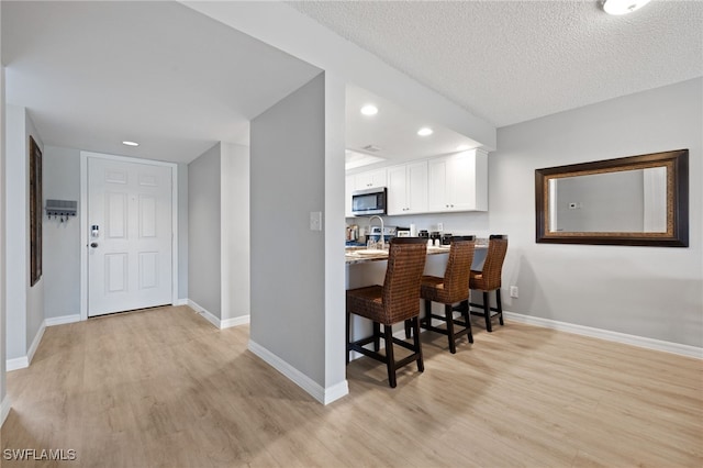 15400 River Vista Dr Unit 304, North Fort Myers, FL 33917 - kitchen featuring light wood-style flooring, stainless steel microwave, white cabinets, and a kitchen breakfast bar