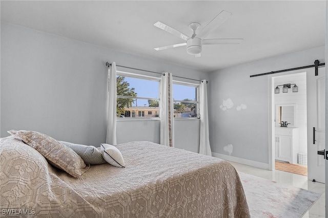 bedroom featuring light tile patterned floors, a barn door, ceiling fan, baseboards, and ensuite bath