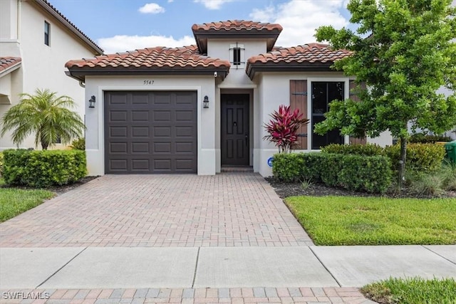 mediterranean / spanish home with a garage, a tiled roof, stucco siding, and decorative driveway