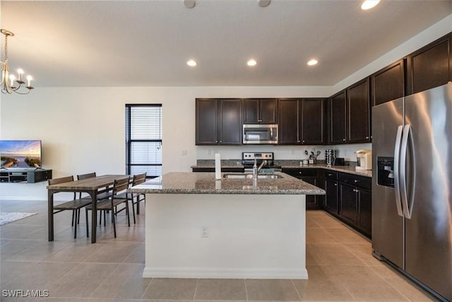 kitchen with a sink, light tile patterned floors, stone countertops, an inviting chandelier, and stainless steel appliances