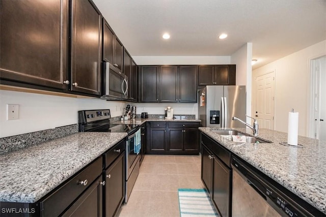 kitchen with appliances with stainless steel finishes, dark brown cabinets, a sink, light tile patterned floors, and light stone counters