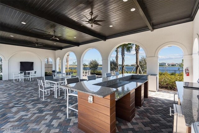 view of patio with a water view, ceiling fan, outdoor wet bar, and fence