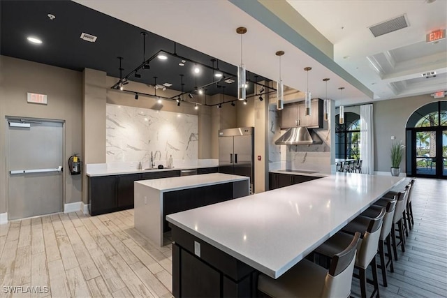 kitchen with light wood-style floors, a center island, light countertops, built in fridge, and dark cabinets