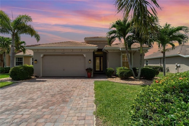 mediterranean / spanish home featuring a garage, stucco siding, a tile roof, and decorative driveway