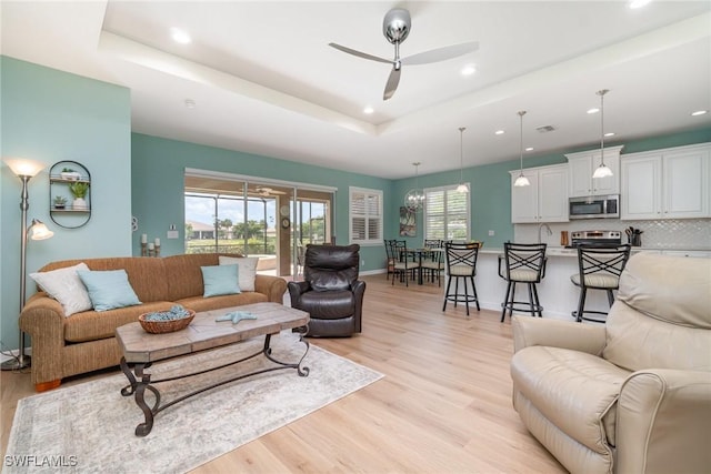 living area with ceiling fan, a raised ceiling, recessed lighting, baseboards, and light wood-type flooring