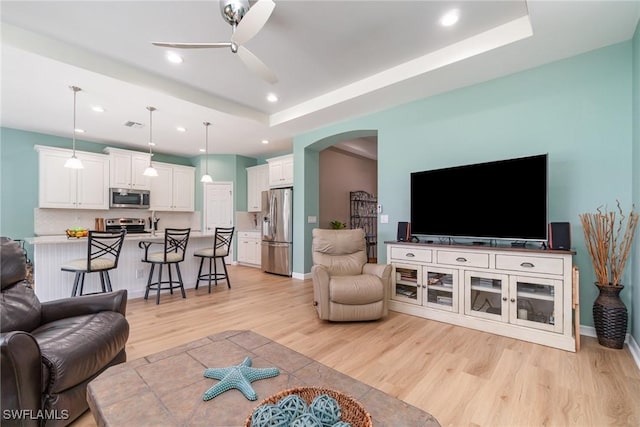 living room with ceiling fan, arched walkways, baseboards, light wood-style floors, and recessed lighting