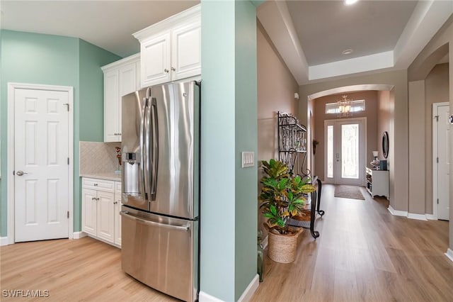 kitchen with stainless steel fridge with ice dispenser, light wood-style floors, arched walkways, white cabinetry, and backsplash