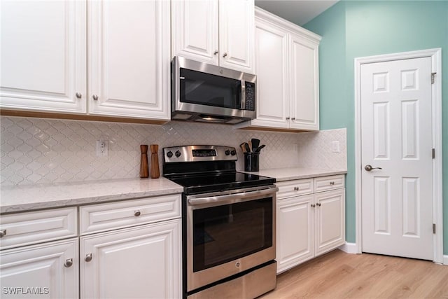 kitchen featuring light stone counters, appliances with stainless steel finishes, light wood-style flooring, white cabinetry, and tasteful backsplash