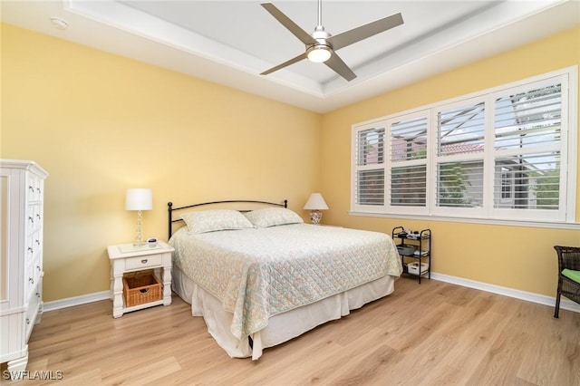 bedroom with baseboards, a ceiling fan, light wood finished floors, and a raised ceiling