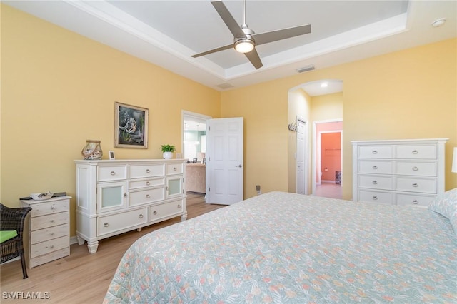 bedroom with a ceiling fan, visible vents, arched walkways, a raised ceiling, and light wood finished floors