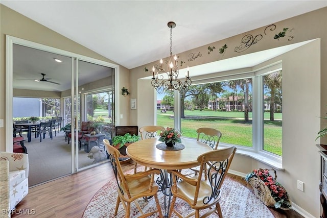 dining space featuring ceiling fan with notable chandelier, wood finished floors, and vaulted ceiling