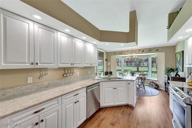 kitchen with a peninsula, white cabinets, stainless steel appliances, and light wood-type flooring