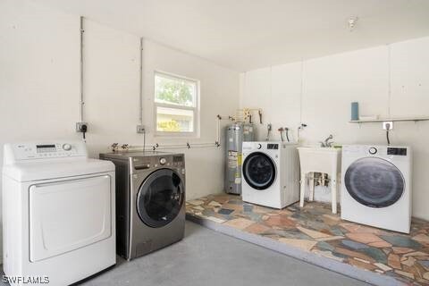 clothes washing area with water heater, washer and clothes dryer, laundry area, and a sink