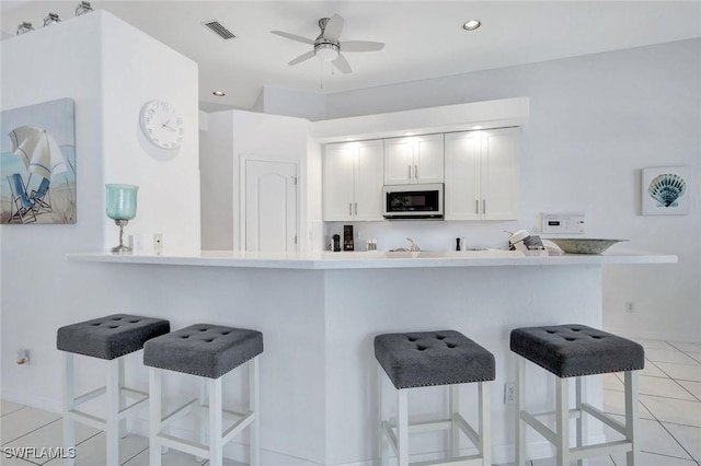 kitchen with ceiling fan, a kitchen breakfast bar, light tile patterned flooring, recessed lighting, and white cabinets