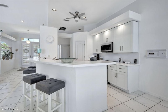 kitchen with a kitchen bar, light tile patterned floors, a ceiling fan, white cabinetry, and light countertops